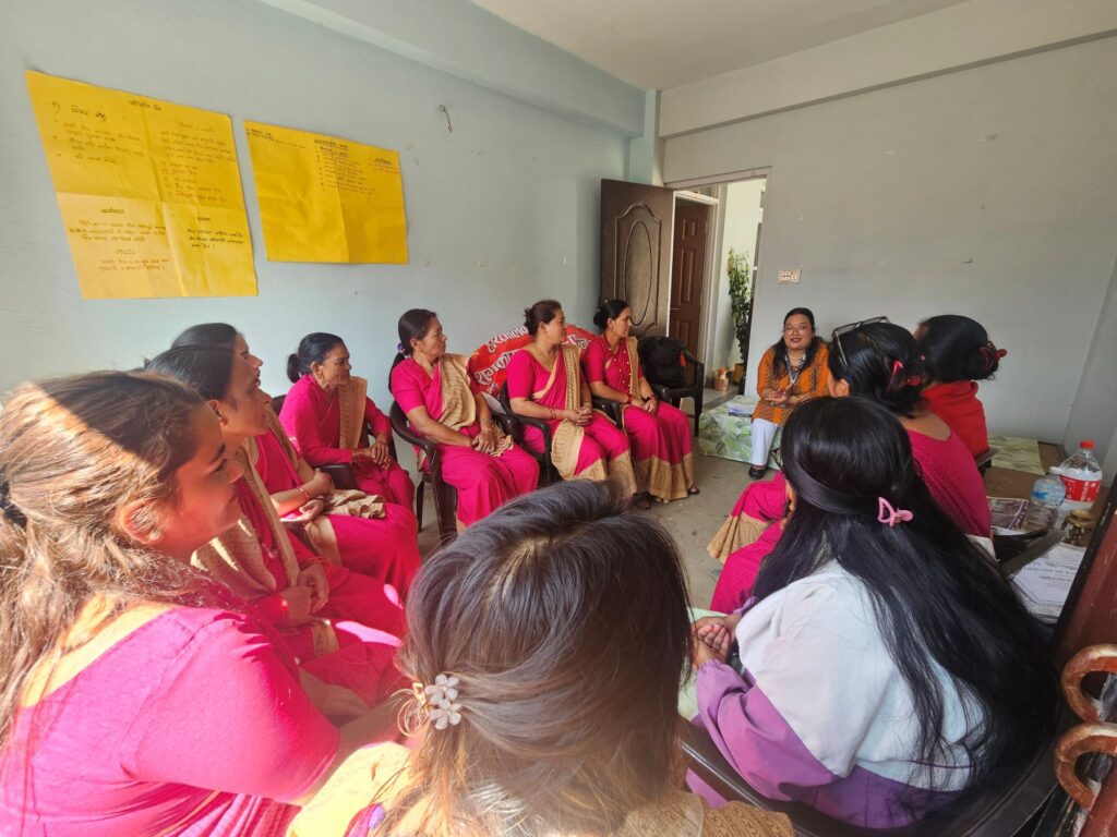 A group of women, most wearing pink clothing, sit in a circle having a discussion focused on peacebuilding in a room with notes posted on the wall.