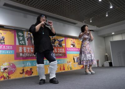 Two performers sing on stage at the One Family Festival 2025, a vibrant multicultural festival with colorful banners and lights illuminating the background.