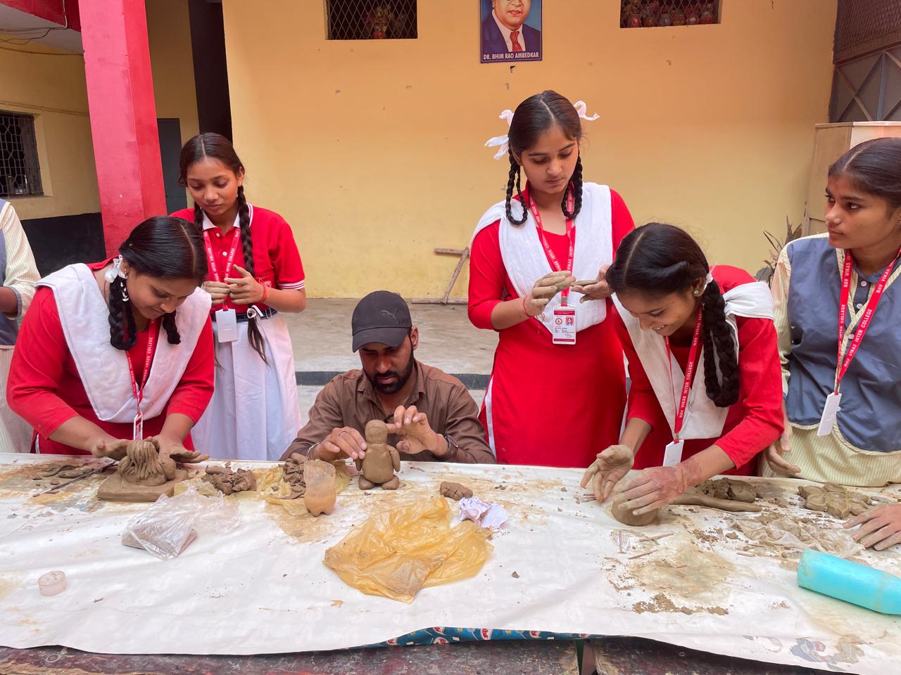 A group of students in red and white uniforms explore clay art with an instructor at a table covered with clay and tools, nurturing student creativity indoors.
