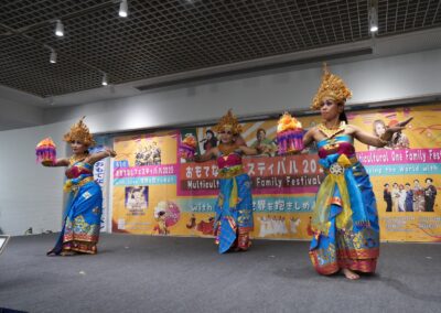 Three women in traditional Balinese attire perform a dance on stage at the 2025 Multicultural Festival, holding colorful offerings.