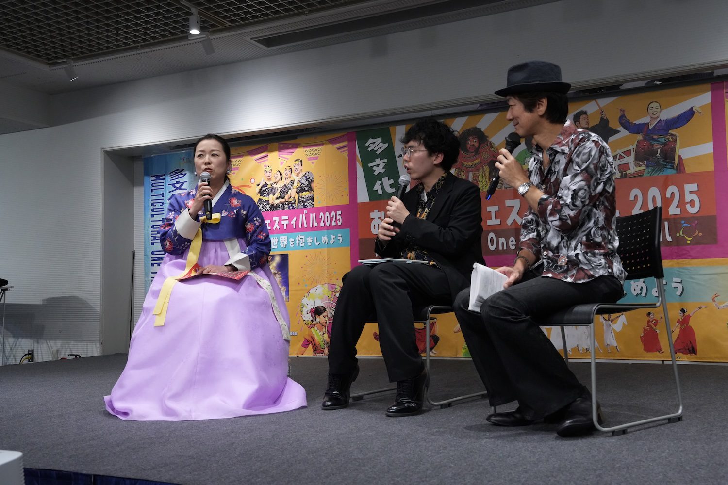 Three people sit on stage having a discussion at the 2025 Family Festival; one woman wears a traditional Korean hanbok, while the two men wear modern clothing, highlighting the event's multicultural atmosphere.