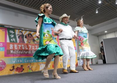 Three adults in colorful traditional attire dance on stage at the 2025 Multicultural Festival, with a vibrant banner in the background.
