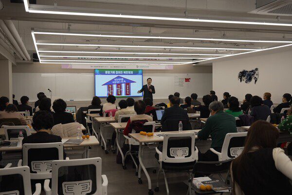 A speaker presents to an audience seated in a classroom, with a slide showing a diagram about the Korean Dream projected on a screen at the front, inspiring discussion on citizen movements and North Korean escapees.