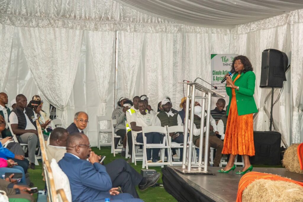 A woman in a green blazer and orange skirt speaks at a podium about the 2025-2030 Strategic Plan to an audience seated inside a white tent at the GPF Africa SMACHS Centre of Excellence.