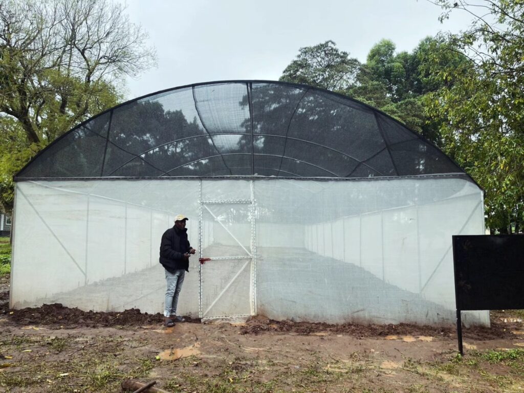 A person stands in front of a large, white, greenhouse structure with a curved roof surrounded by trees and vegetation, highlighting environmental stewardship within a lush setting.