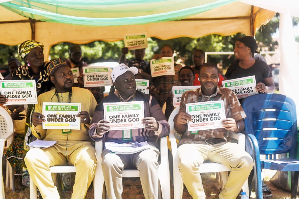 A group of people sit under a tent holding signs that read