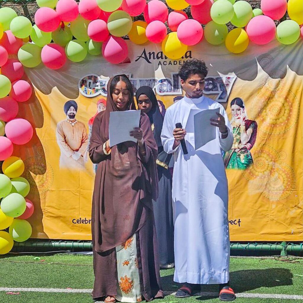 Three future leaders stand on a stage holding papers and a microphone, with colorful balloons and a banner reading