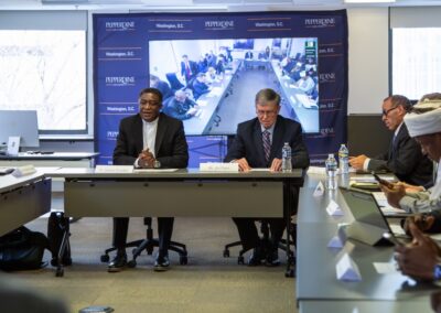 A group of people, including Nigerian faith leaders, sit around a conference table, with two men in the center and a large video screen in the background displaying a remote meeting addressing violence and insecurity.