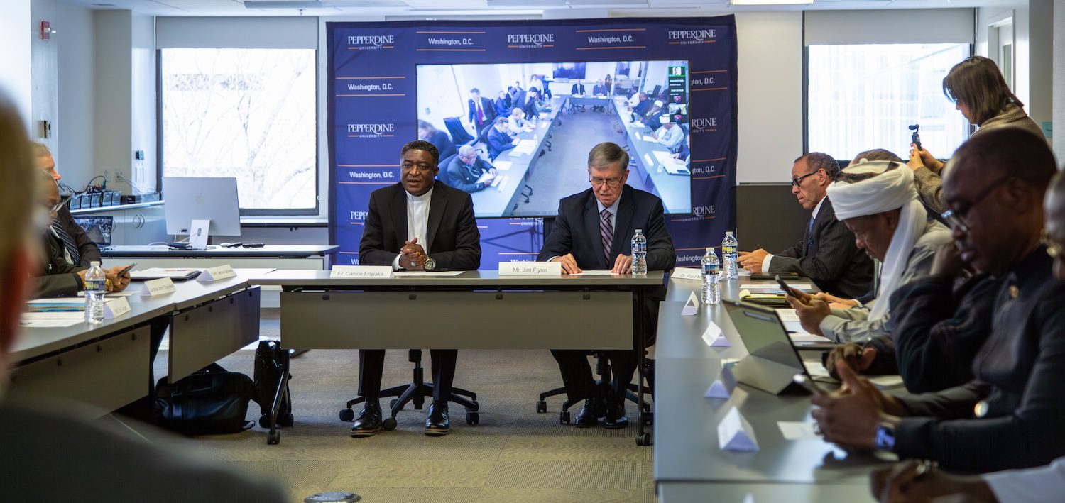 A group of people, including Nigerian faith leaders, sit around a conference table, with two men in the center and a large video screen in the background displaying a remote meeting addressing violence and insecurity.