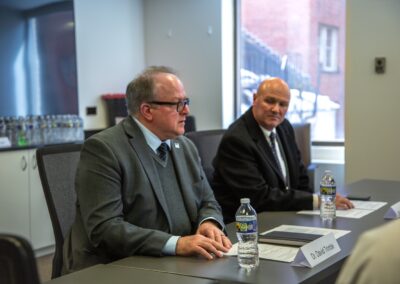 Two men in suits sit at a conference table in Washington D.C., engaged in dialogue on International Religious Freedom, with bottled water, papers, and name cards in a modern meeting room.