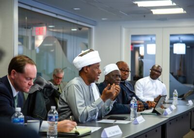 A group of men in business attire sit at a conference table in Washington D.C., engaged in dialogue; bottled water, papers, and name tags are visible on the table.