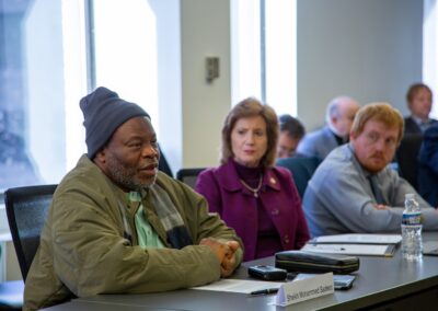 A man in a beanie and jacket sits at a conference table in Washington D.C., speaking as part of an International Religious Freedom dialogue; others are seated beside him, and his nameplate reads "Sheikh Mohamed Saliou.