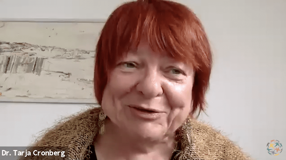 A woman with short red hair smiles during a video call. The text 
