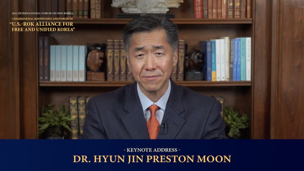 Dr. Hyun Jin Preston Moon delivers a keynote address, seated in front of a bookshelf, wearing a suit and tie, with event details displayed on the screen.