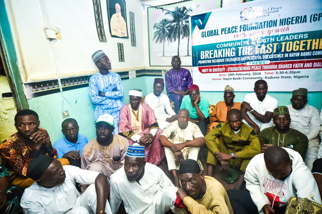 A group of men pose for a photo in front of a banner for an Interfaith Fast-Breaking peace event at the Hayin Banki Community in Kaduna State, Nigeria, organized by GPF Nigeria.