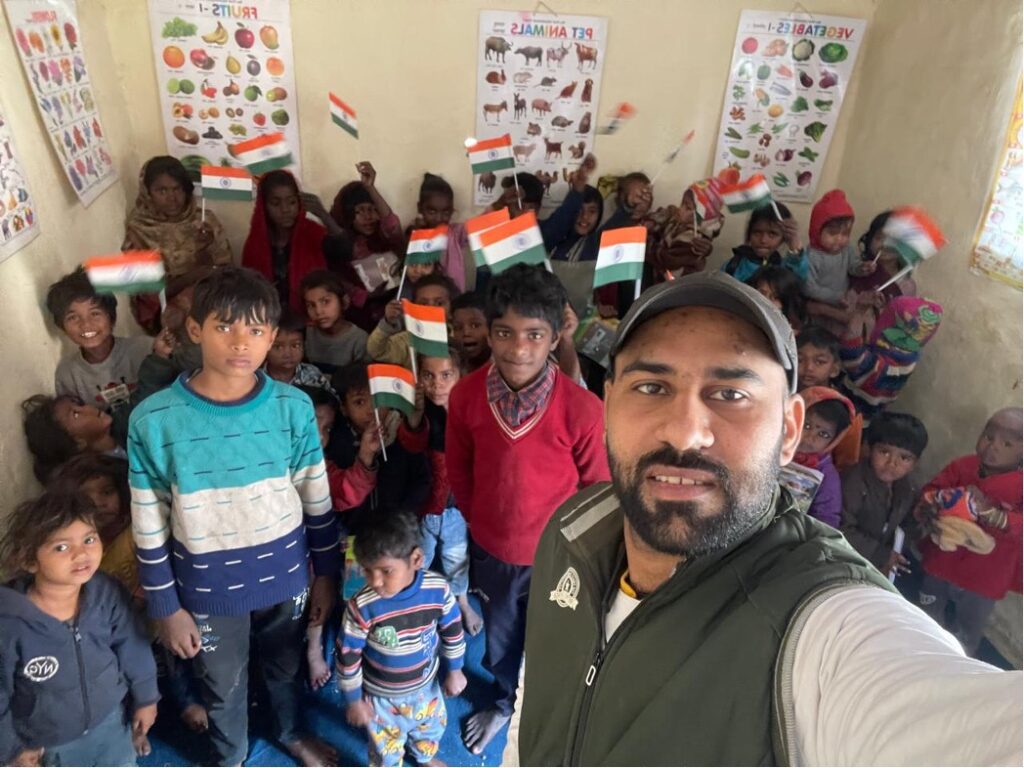 A man takes a selfie in a classroom during Republic Day 2026, with children holding Indian flags, educational posters on the walls, and students gathered around him, celebrating civic education and community engagement.
