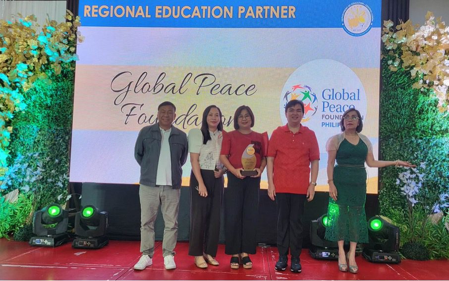 Five people stand on stage with an award, in front of a screen displaying