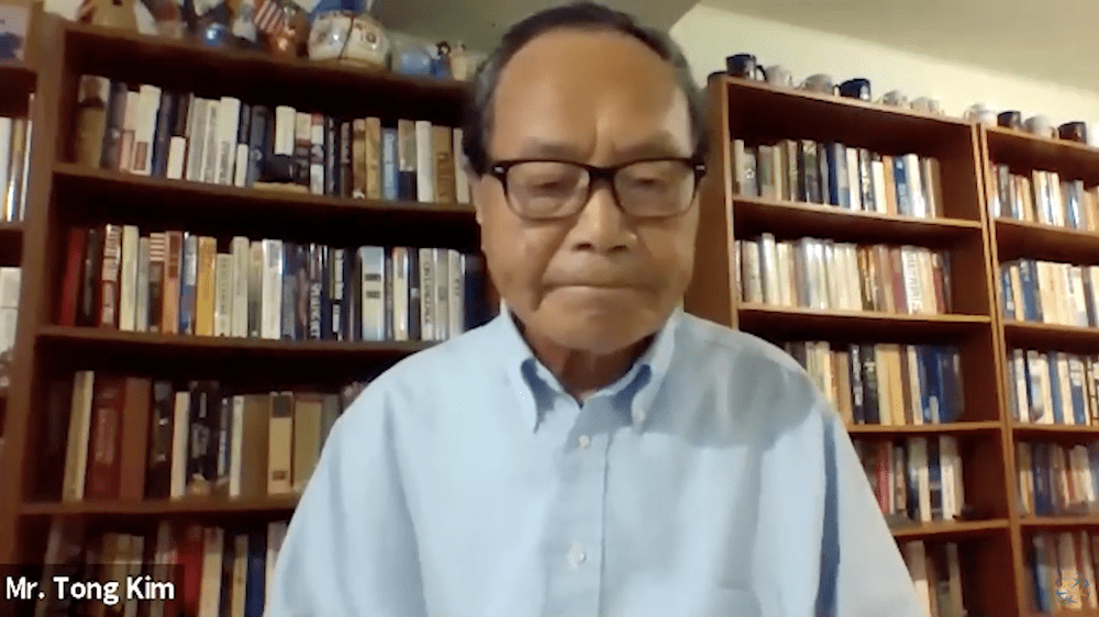 An older man wearing glasses and a light blue shirt sits in front of bookshelves during a video call about the denuclearization of the Korean Peninsula. Text on screen reads 