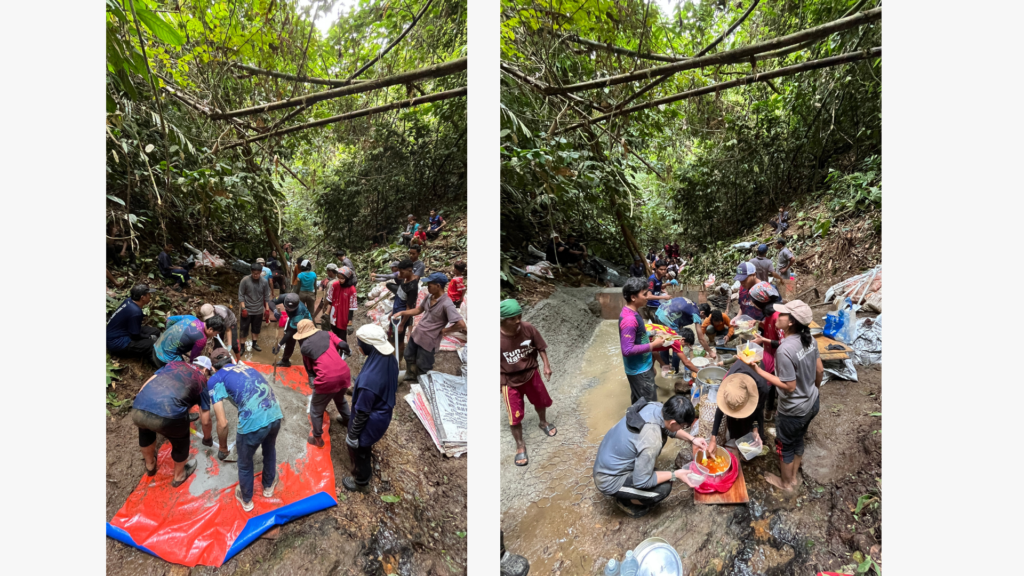 Groups of people work together in a forested area near Kuala Lipisment, sifting and washing gritty materials in muddy water and on tarps, surrounded by dense vegetation.