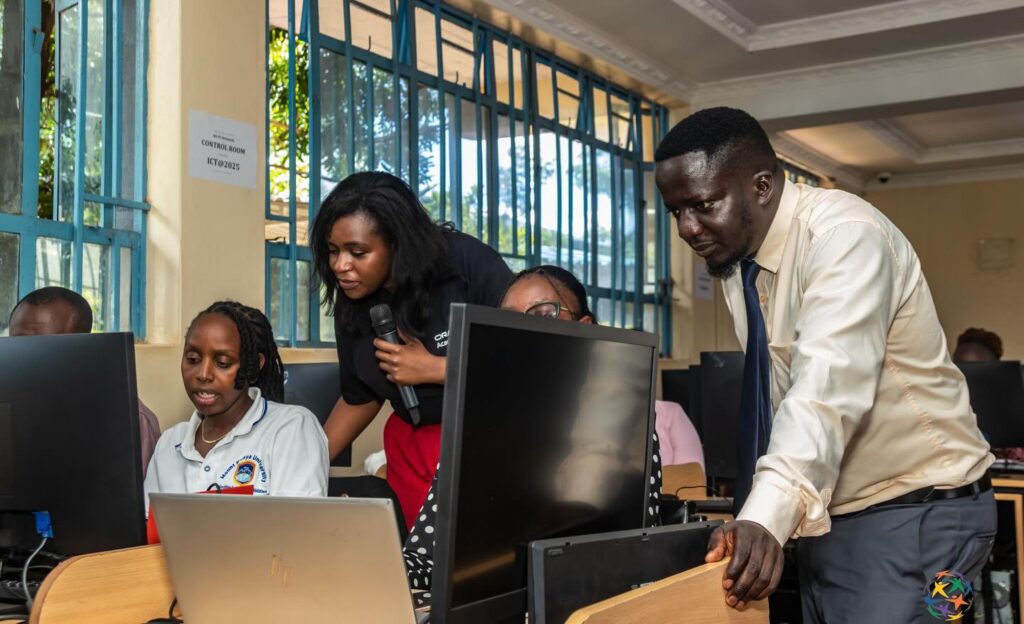 A man and a woman assist students working on desktop computers in a classroom with large windows during a computer training session focused on AI and Cloud Skills as part of the Oracle Academy program at GPF Kenya.