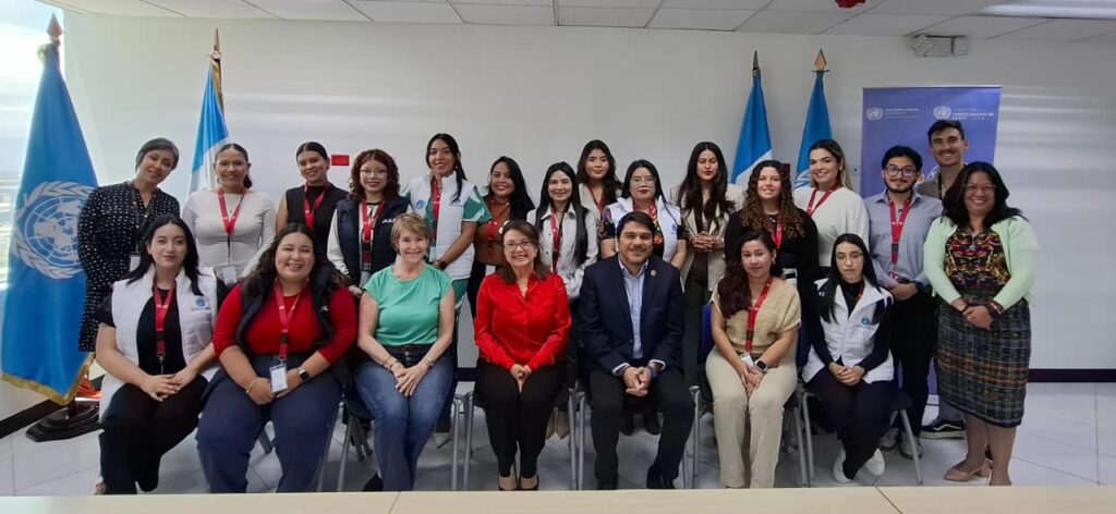 A group of people pose for a photo in an office setting, with United Nations flags and a UN banner in the background, highlighting their commitment to Democratic Resilience and Youth Digital Leadership in Guatemala.