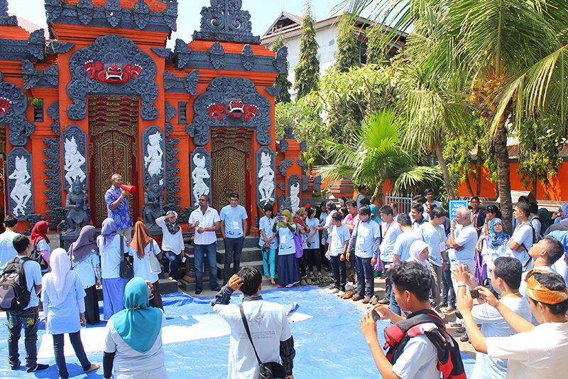 People clapping and smiling at a formal event inside a room with decorative banners celebrating holistic learning in the background.