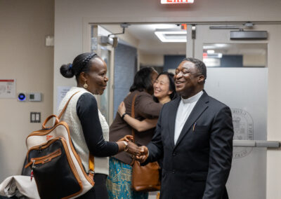 Two people shake hands and smile near an open doorway at the Africa Summit Gallery, while two others from the Ubuntu Africa Diaspora embrace in the background.
