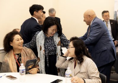 A group of professionally dressed adults interact and smile together around a table in the Capitol Forum Policy Gallery, creating an engaging atmosphere in the conference room.