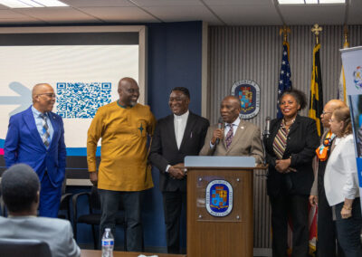 A group of people in formal attire stand at a podium during an indoor event, with a QR code displayed on a screen in the background at the Ubuntu Africa Diaspora Summit.