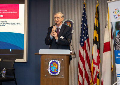 An older man in a suit speaks at a podium with microphones, standing in front of flags and a presentation screen during the Ubuntu Africa Diaspora Summit in a conference room.