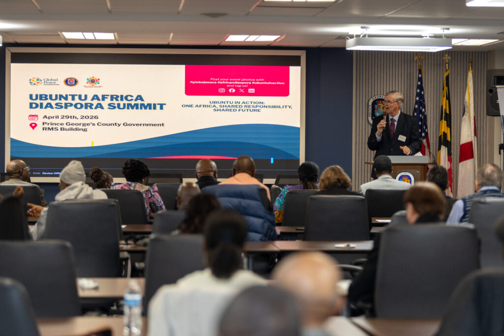 A speaker addresses attendees at the Ubuntu Africa Diaspora Summit 2026, with event details displayed on a large screen in the conference room, capturing a moment worthy of any gallery.