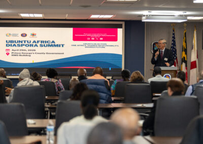 A speaker addresses attendees at the Ubuntu Africa Diaspora Summit 2026, with event details displayed on a large screen in the conference room, capturing a moment worthy of any gallery.