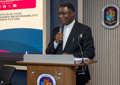 A man in a suit speaks into a microphone at a podium with the Prince George’s County, Maryland seal, in front of a screen displaying an Africa Diaspora Summit 2026 presentation.