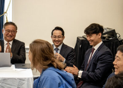 A group of people in business attire sit and smile around a table during a Capitol Forum Policy Gallery event, with laptops and equipment visible in the background.