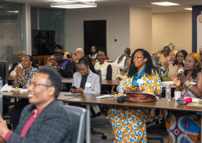 A group of people sit at tables in a conference room, listening and clapping, with notebooks, cups, and water bottles on the tables at the Diaspora Summit 2026.
