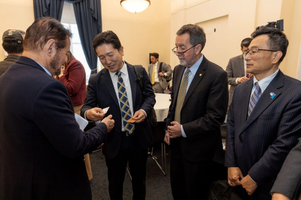 Four men in business attire stand together in a conference room at the Capitol Policy Forum April 2026, exchanging business cards and conversing.