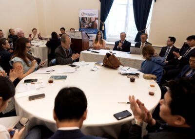 A group of people in business attire sit and clap around a large round table during the Capitol Policy Forum April 2026, held in a well-lit room as part of a formal meeting or conference.