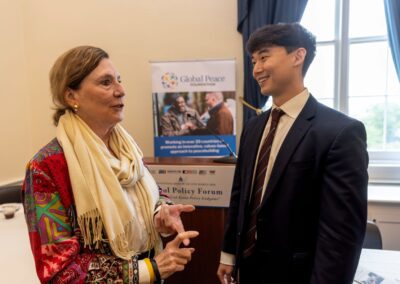 Two people converse in front of a "Global Peace Foundation" poster at an indoor event, both dressed in business attire during the International Forum on One Korea.