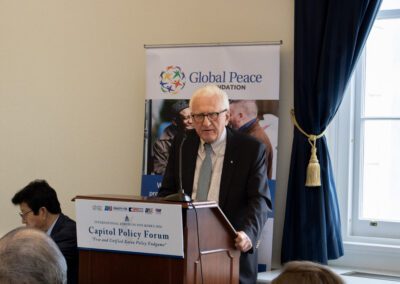 An older man speaks at a podium during a Capitol Policy Forum event, with a Global Peace Foundation banner behind him, highlighting discussions on Korean unification at the International Forum on One Korea.