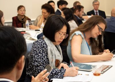 Attendees at the International Forum on One Korea sit at tables in a seminar room, attentively taking notes and listening to a speaker just out of frame.