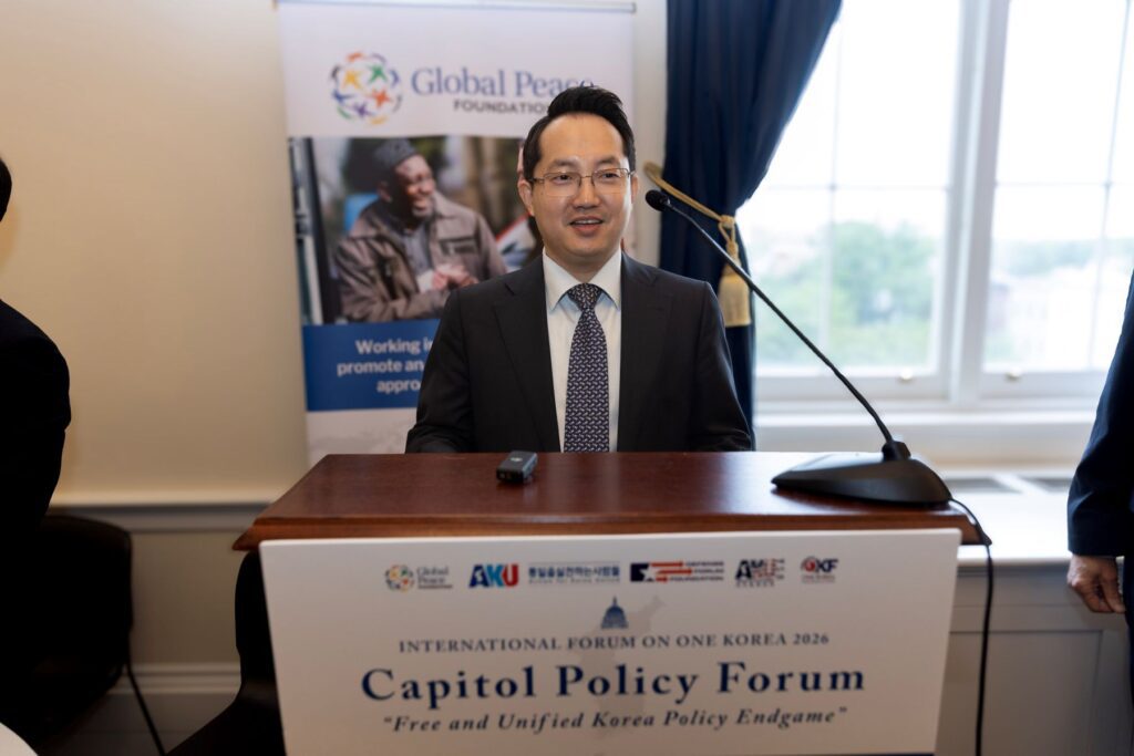 A man in a suit stands at a podium labeled 