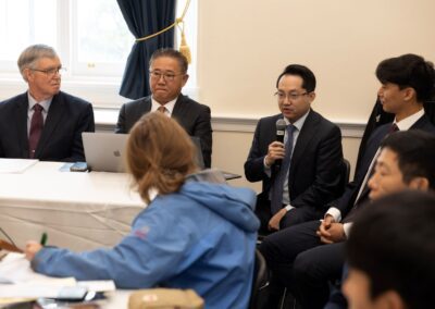 Four men in business attire sit at a table, one speaking into a microphone—sharing Hyunseung Lee’s story of escape and freedom—as others listen intently and people in the foreground take notes.