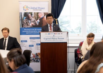 A man speaks at a podium during a Capitol Policy Forum event, with an International Forum on One Korea banner behind him and attendees seated on either side.