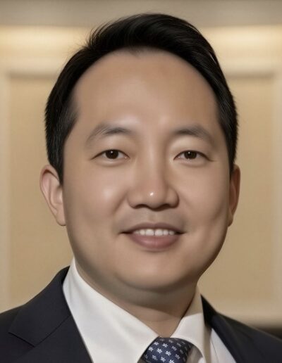 Hyun-Seung Lee, dressed in a suit and tie, smiles at the camera while standing indoors against a blurred, neutral background.