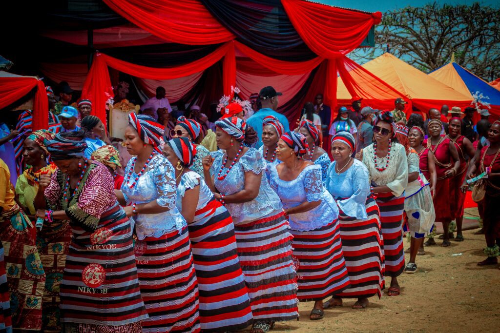 A group of women in matching striped skirts and headwraps dance in a procession at the Dung Nikyob Cultural Festival, celebrated under red and black canopies, promoting Peace in Southern Kaduna before a lively crowd.