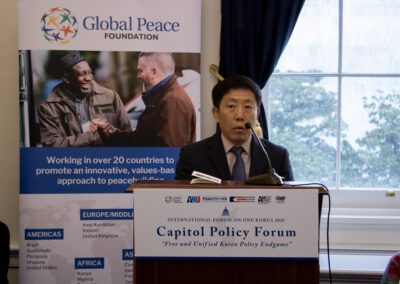 A man speaks at a podium during the Capitol Policy Forum, part of the International Forum on One Korea, with a Global Peace Foundation banner and a window in the background.