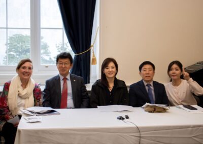 Five people sit at a table with papers and microphones in front of them, posing for a group photo during the International Forum on One Korea in a room with a window and dark curtains.
